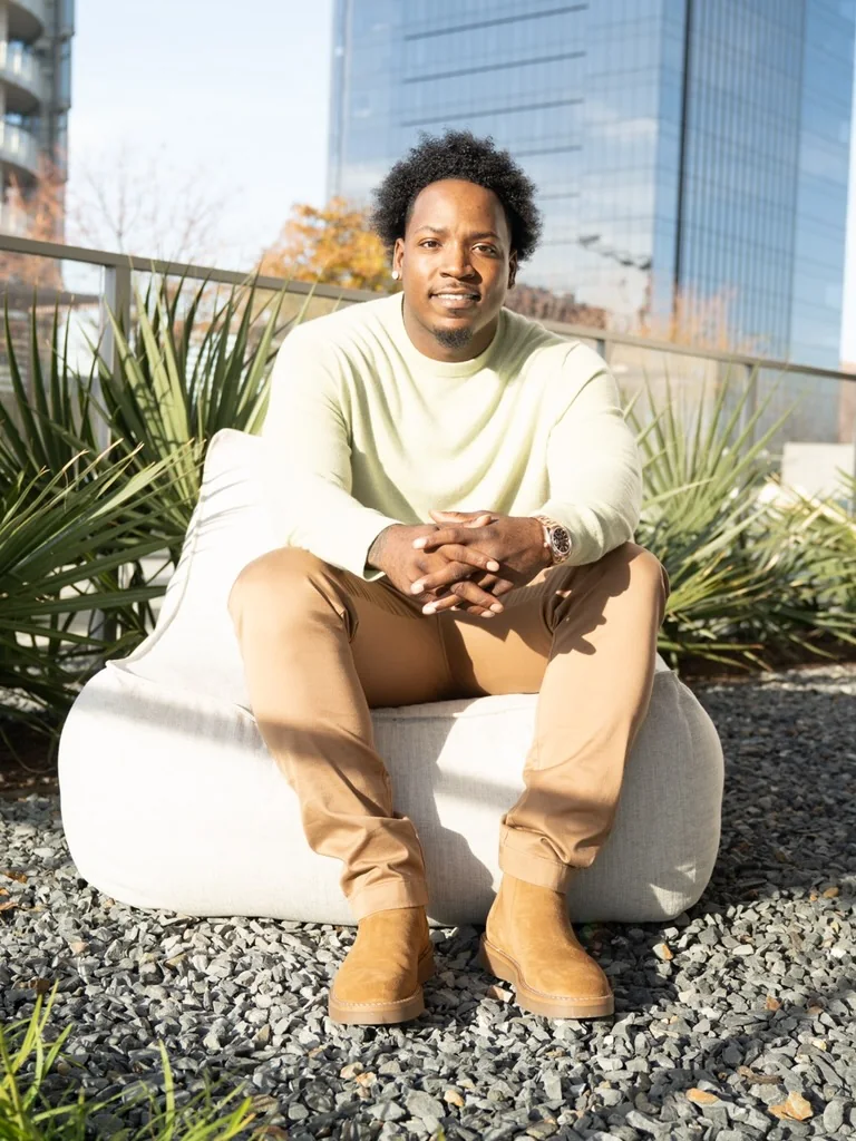 Jet seated outdoors on a rooftop terrace, city towers behind him